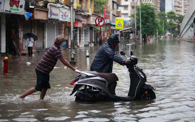 The BMC also asked people to stay away from broken electric poles, sewage, gutters, debris, and exposed power lines and keep necessary documents in water-proof bags and packets.
In picture: A man helps a motorist by pushing his scooter that got stuck in an inundated road in Sion.