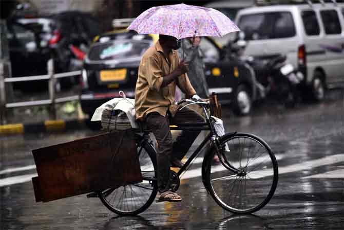 In picture: A man rides a bicycle through a flooded road, while balancing his umbrella, in Sion