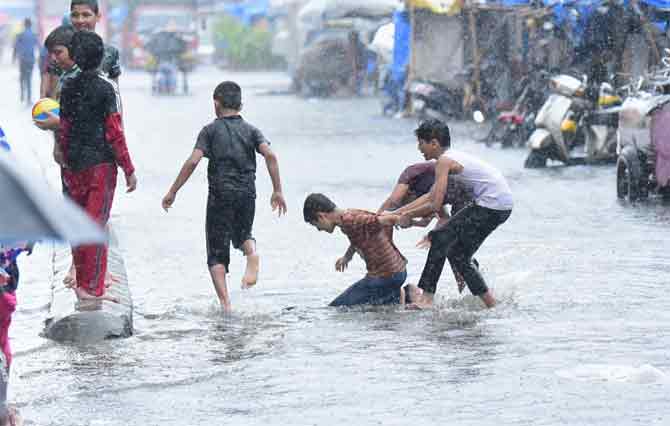 In picture: Children play in the rain on a waterlogged street in Kumbharwada