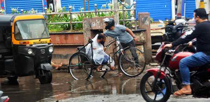 A man helps a differently-abled person whose wheelchair got stuck during heavy rains.
