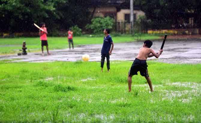 Children enjoy the rains while playing cricket at a ground in Antop Hill.