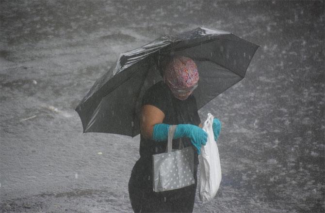 In photo: A woman armed with mask and gloves waits for a bus during heavy rainfall.