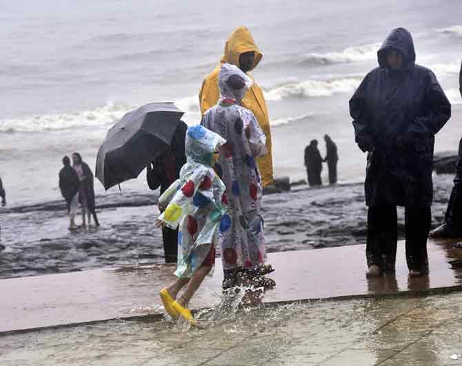 In photo: A child wearing a raincoat enjoying the weather at seashore.