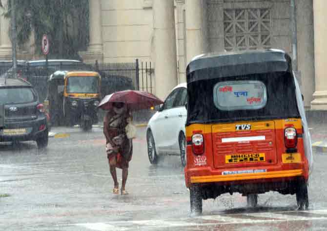 In photo: A woman walks through a busy road during heavy rain.