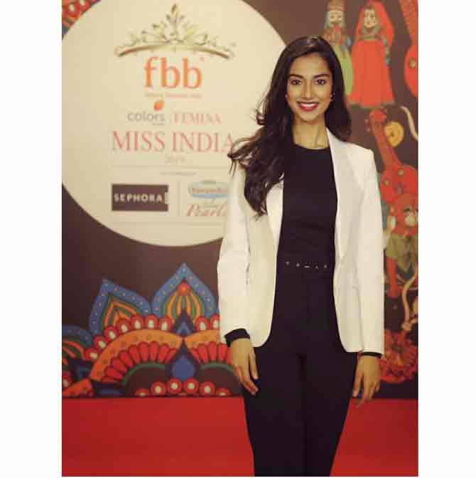 Miss Grand International 2018 1st runner-up Meenakshi Choudhary is all smiles as she poses for shutterbugs at a public event wearing a plain black top, a pair of black trousers and a white blazer. 
