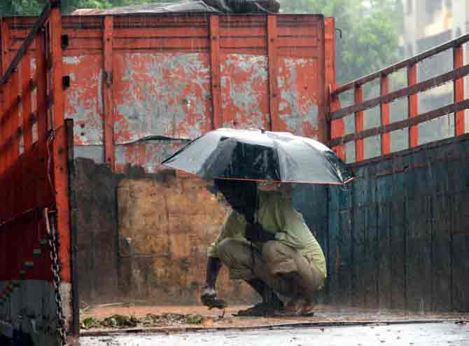 Amid heavy showers, a man, taking shelter under an umbrella, cleans his truck in Bhayander.