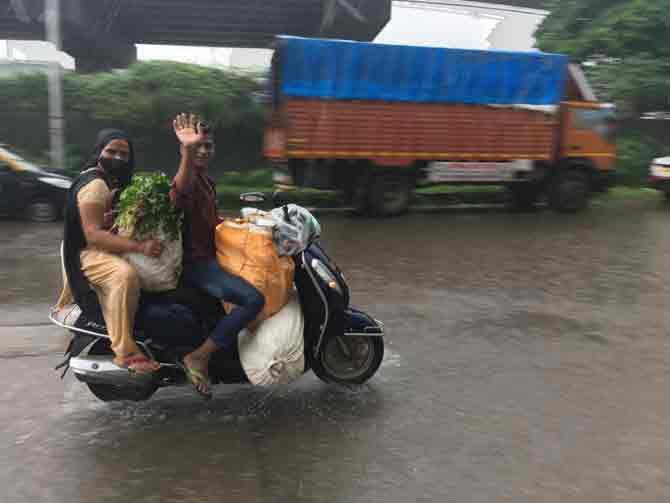 A motorist smiles and waves at the camera while riding a two-wheeler in Wadala amid heavy showers.