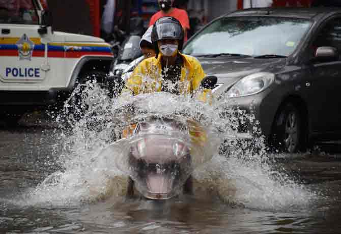 A motorist splashes water while riding his bike through a water-logged road.