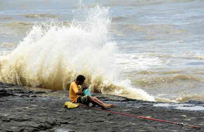 A fisherman sits near the seashore in Bandra as a huge wave hits the shore.