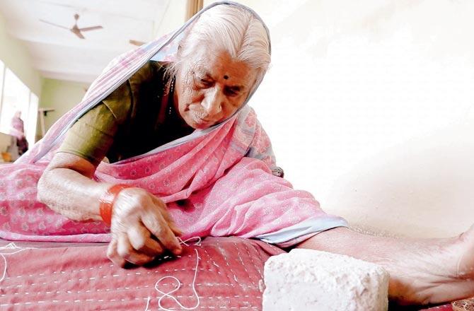 An elderly woman stitches a quilt