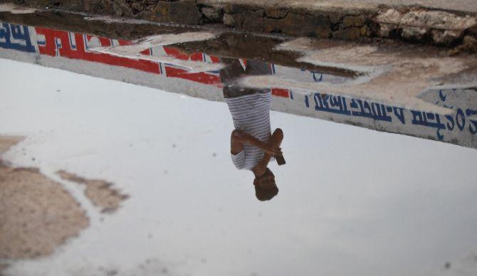 In photo: A man's reflection captured through the water accumulated by the first showers of rains amid lockdown in the city.