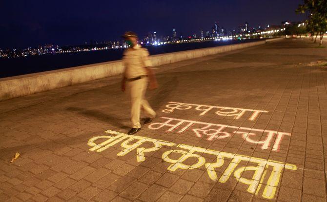 In photo: A police personnel walks past a printed message at Marine Drive in South Mumbai, the message urges citizens to wear face masks.