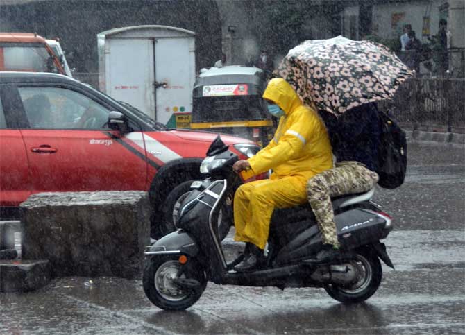 In picture: Social distancing goes for a toss! A motorist tries to ride his bike in the rain as the pillion rider tries to protect himself with an umbrella.