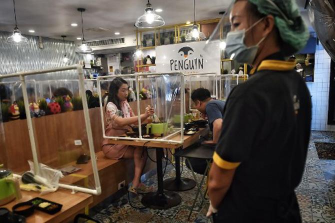 A waiter wearing a face masks looks on as people eat in between plastic partitions, set up in an effort to contain any spread of the COVID-19 coronavirus, at the Penguin Eat Shabu hotpot restaurant in Bangkok.