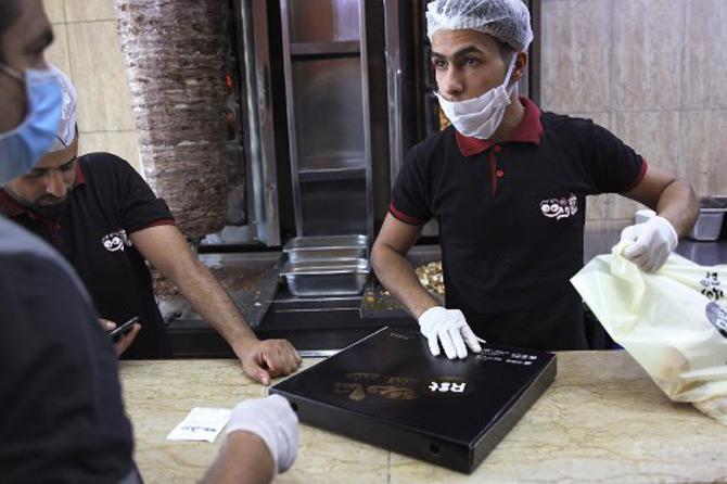 A worker, clad in mask and latex gloves for safety during the COVID-19 coronavirus pandemic, prepares to wrap a prepared iftar (fast-breaking) meal at a fast-food restaurant in Iraq's capital Baghdad before curfew time during the Muslim holy fasting month of Ramadan.