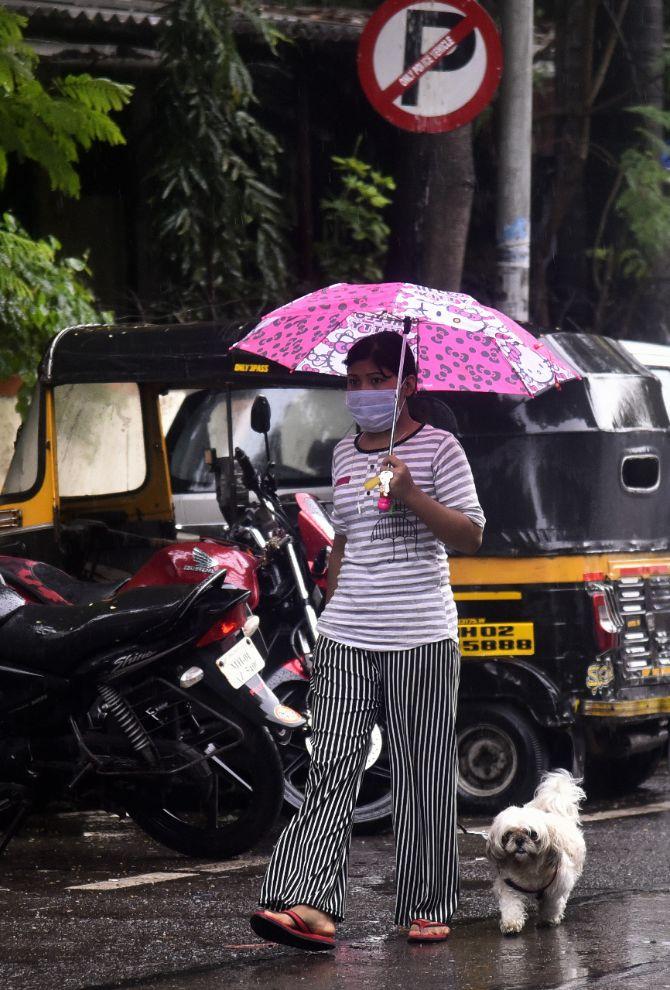 In photo: A young woman wearing face mask and carrying an umbrella was seen strolling her pet on the streets of Bandra.