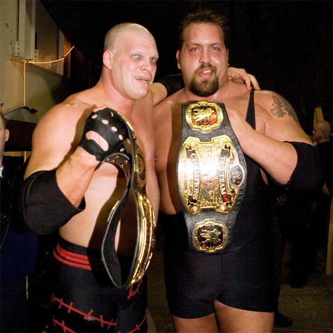 WWE superstars Kane and The Big Show pose with the WWE tag team titles. Both giant superstars were pivotal to the WWE over 3 decades. They won the tag team titles twice.