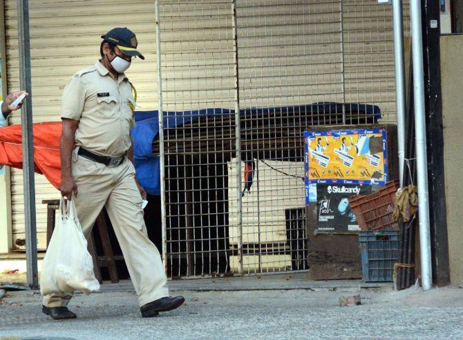 In photo: A Mumbai Police personnel walks back home after buying groceries during total lockdown in the city.