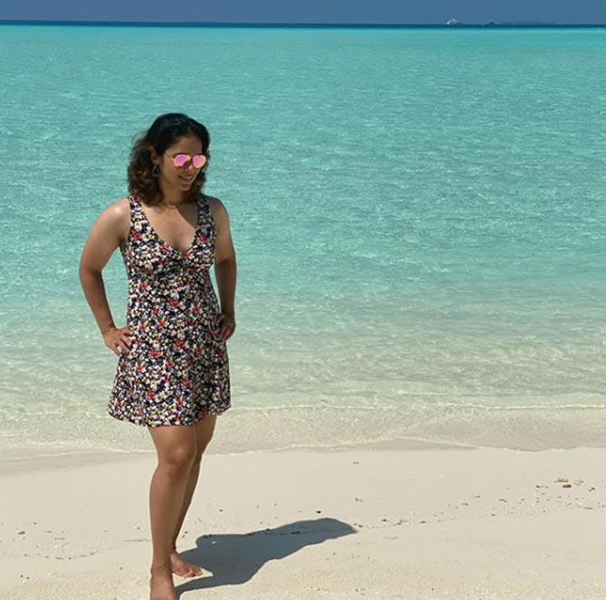 Saina Nehwal poses in a printed short dress by the beach with stylish pink tinted sunglasses.