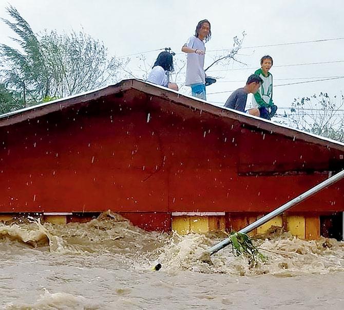 Residents stand on their house’s roof after a river overflowed on Sunday. Pics/AFP