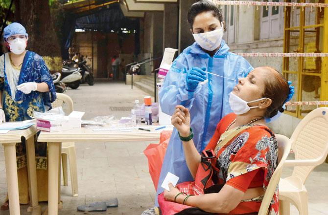 A medic collects a swab sample for COVID-19 test at Jain Health care centre in Dadar West. File pic/Suresh Karkera