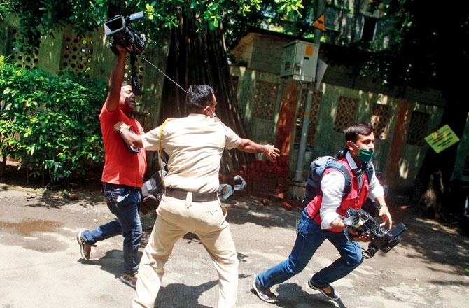 A policeman spars with video cameramen trying to take pictures of Showik Chakraborty, Sushant Singh Rajput