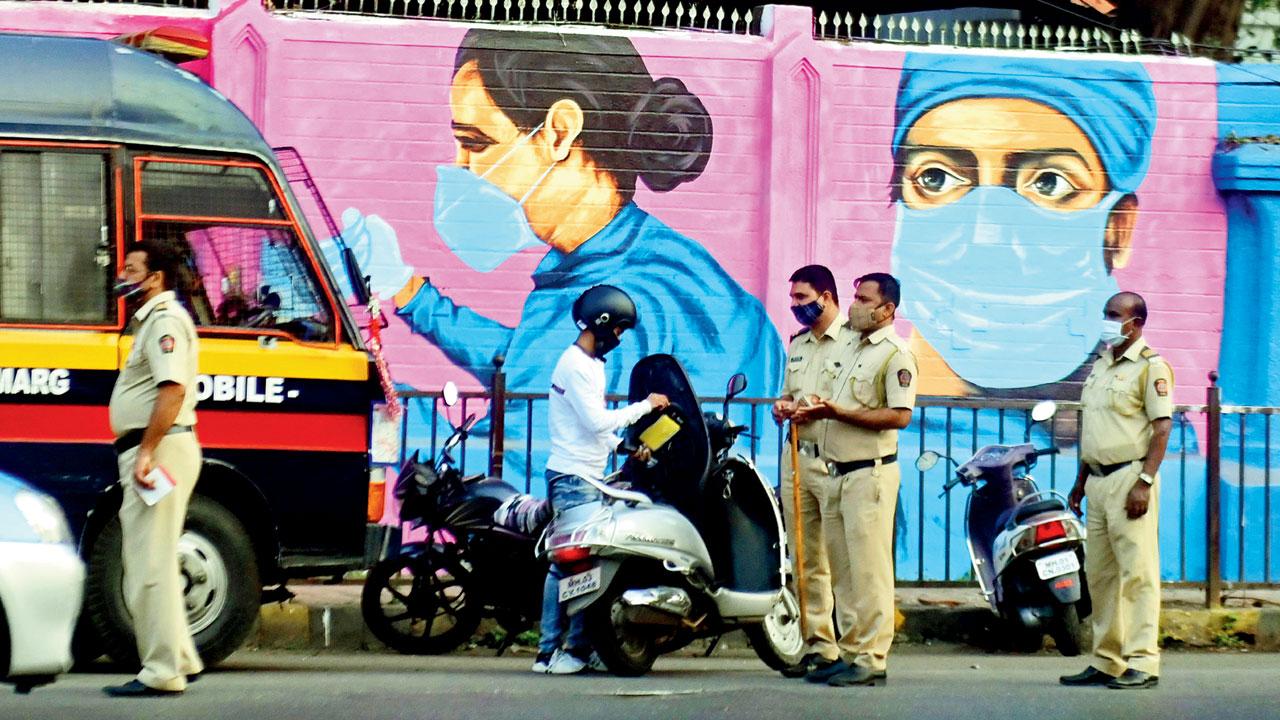 Cops check a bike at Nagpada junction, in the backdrop of a mural stressing the need for masks, on Sunday. Pic/Bipin Kokate