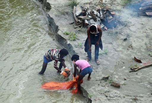 3) Floating bodies 
On May 8, among the first of hundreds of floating and buried bodies of suspected Covid-19 victims were seen by the banks of Ganges River in Uttar Pradesh’s Sujabad. The disturbing sight did not end there. Over the month, more than 100 bodies were recovered from the Ganges in Bihar and Uttar Pradesh. This was the time when Uttar Pradesh and Bihar were daily recording over 25,000 and 7,000 Covid-19 cases, respectively.
Photo caption: Municipal corporation workers move a body buried in a shallow grave on the banks of the Ganges river during the Covid-19 pandemic as they cremate other bodies buried there to prevent them from floating downstream near Phaphamau Ghat, in Allahabad on June 25, 2021.
