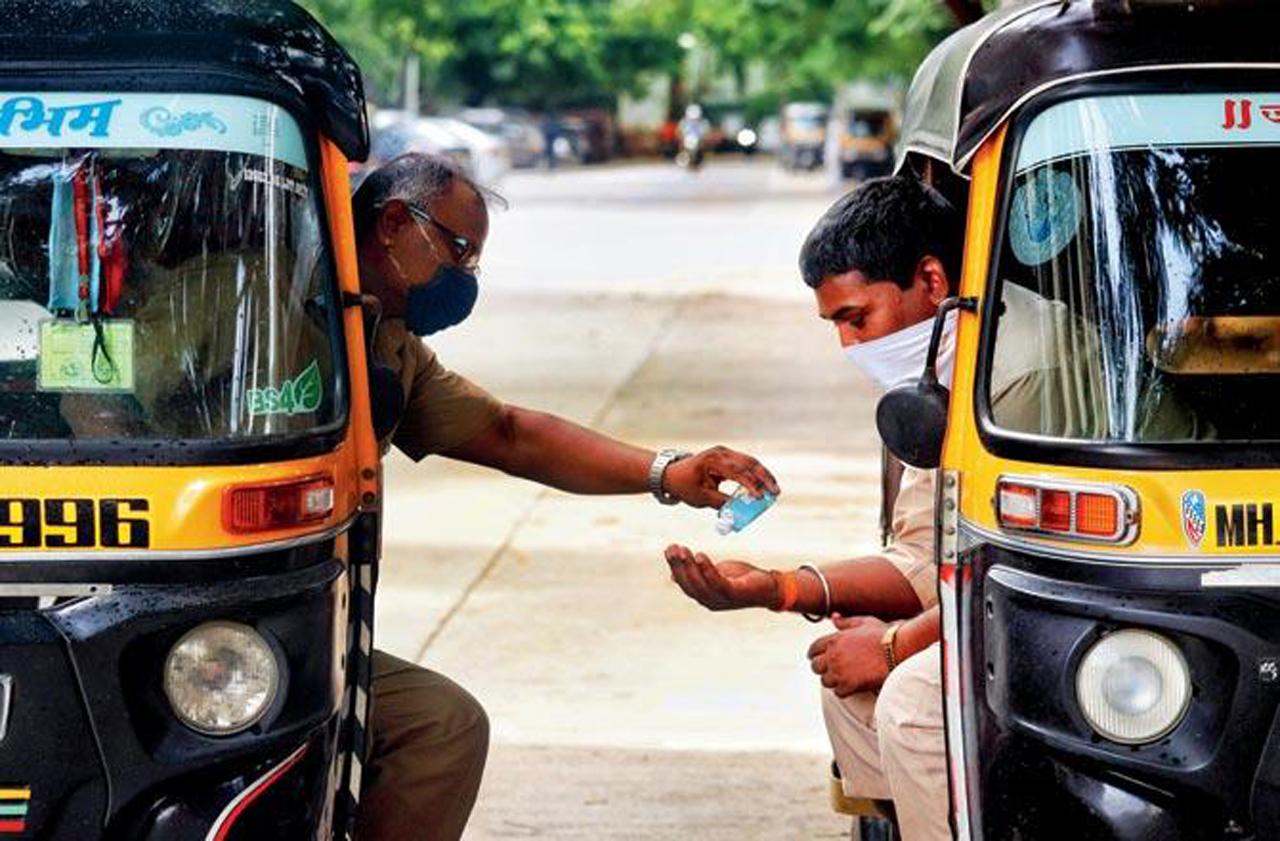 An auto-driver shares his hand sanitiser with another fellow driver. Pic/Anurag Ahire
