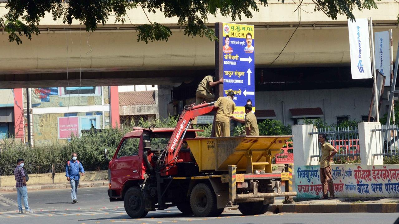 In picture: BMC workers remove illegal posters put on a signboard at Western Express Highway in Kandivli amid lockdown-like curfew in Mumbai. Photo: Satej Shinde