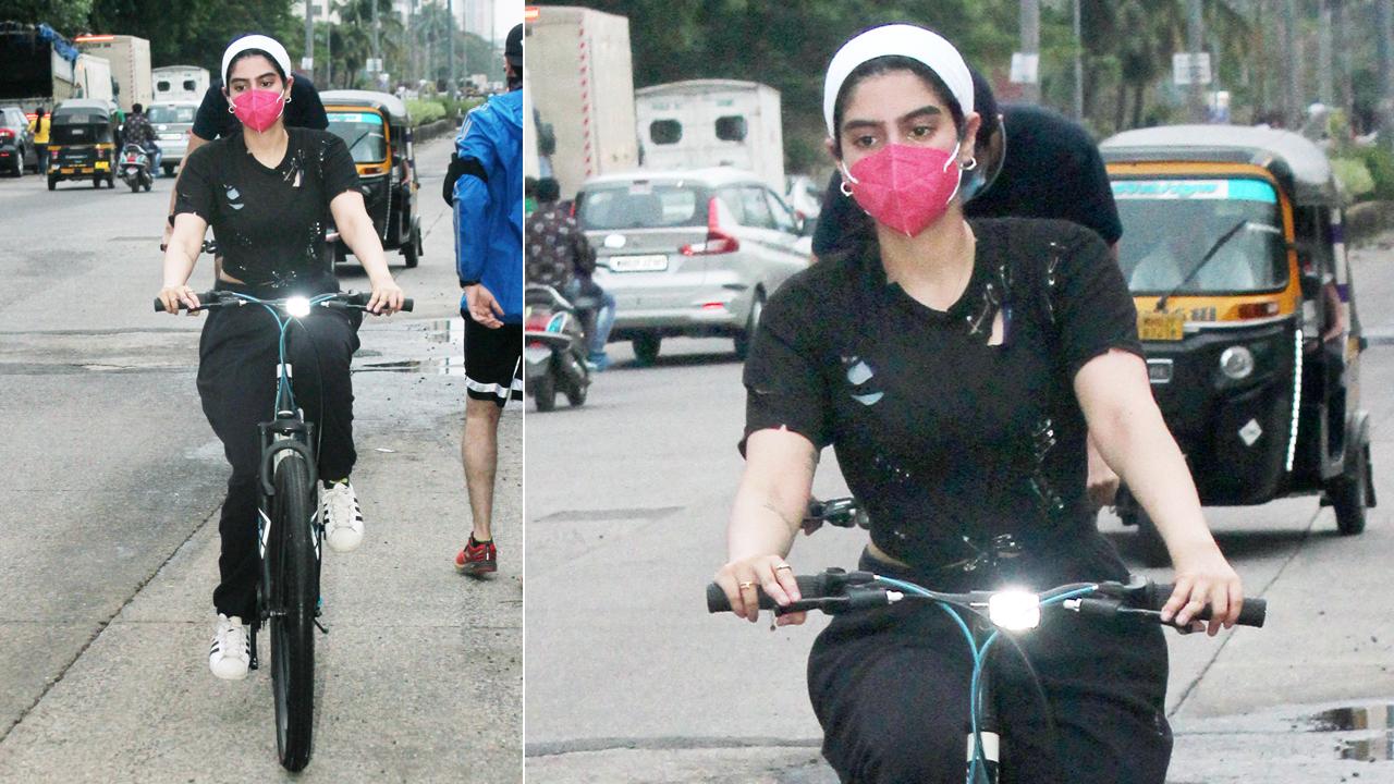 Khushi Kapoor was clicked while cycling on the streets of Bandra, a few minutes away from her residence. Khushi was snapped in an all-black attire - t-shirt and track pant, paired with a pink mask and white headband.