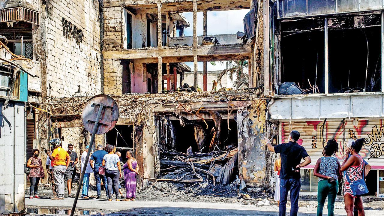 Residents, elected officials and journalists in front of a burnt building on the French island of Guadeloupe, after days of protests. Pics/AFP