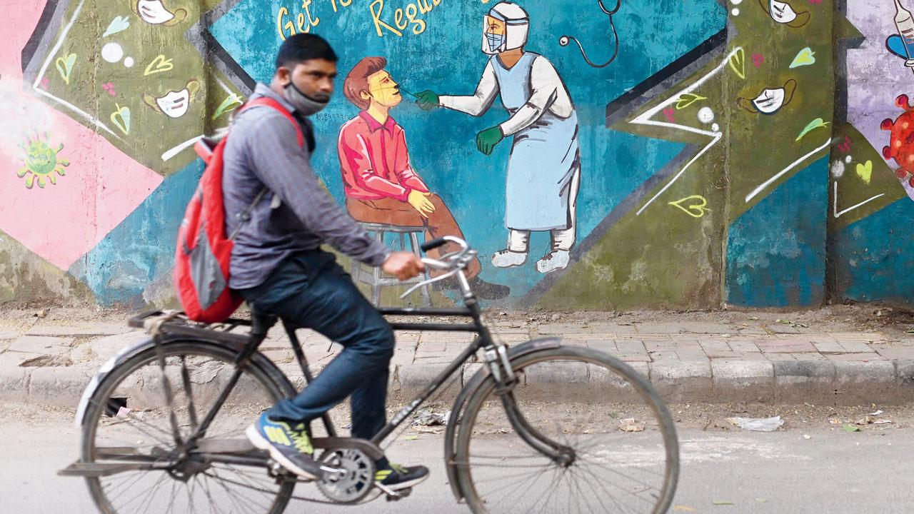 A cyclist rides past a mural depicting COVID testing in New Delhi. Pic/AFP