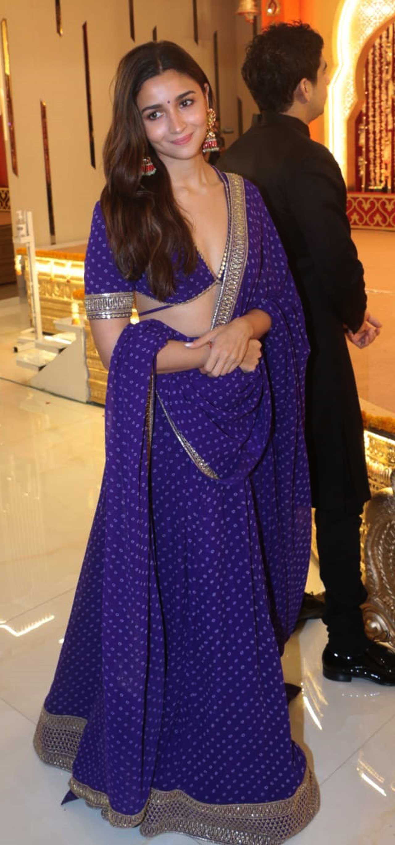 Alia Bhatt was the cynosure of all eyes as she stepped out with Ranbir Kapoor and Ayan Mukerji to attend Lakshmi Puja in the city. The actress wore a printed purple Sabyasachi lehenga set, that had a plunging neckline on a half sleeve, backless blouse adorned with polka print and tied with a dori behind. Gold embroidery on sleeves and an embellished hemline, a matching printed dupatta with patti embroidery completed the outfit. Pink and gold colour jhumkis, a matching bindi for accessories, minimal make-up with a blush pink lip colour, sleek eyeliner, and blushed cheeks completed her look.