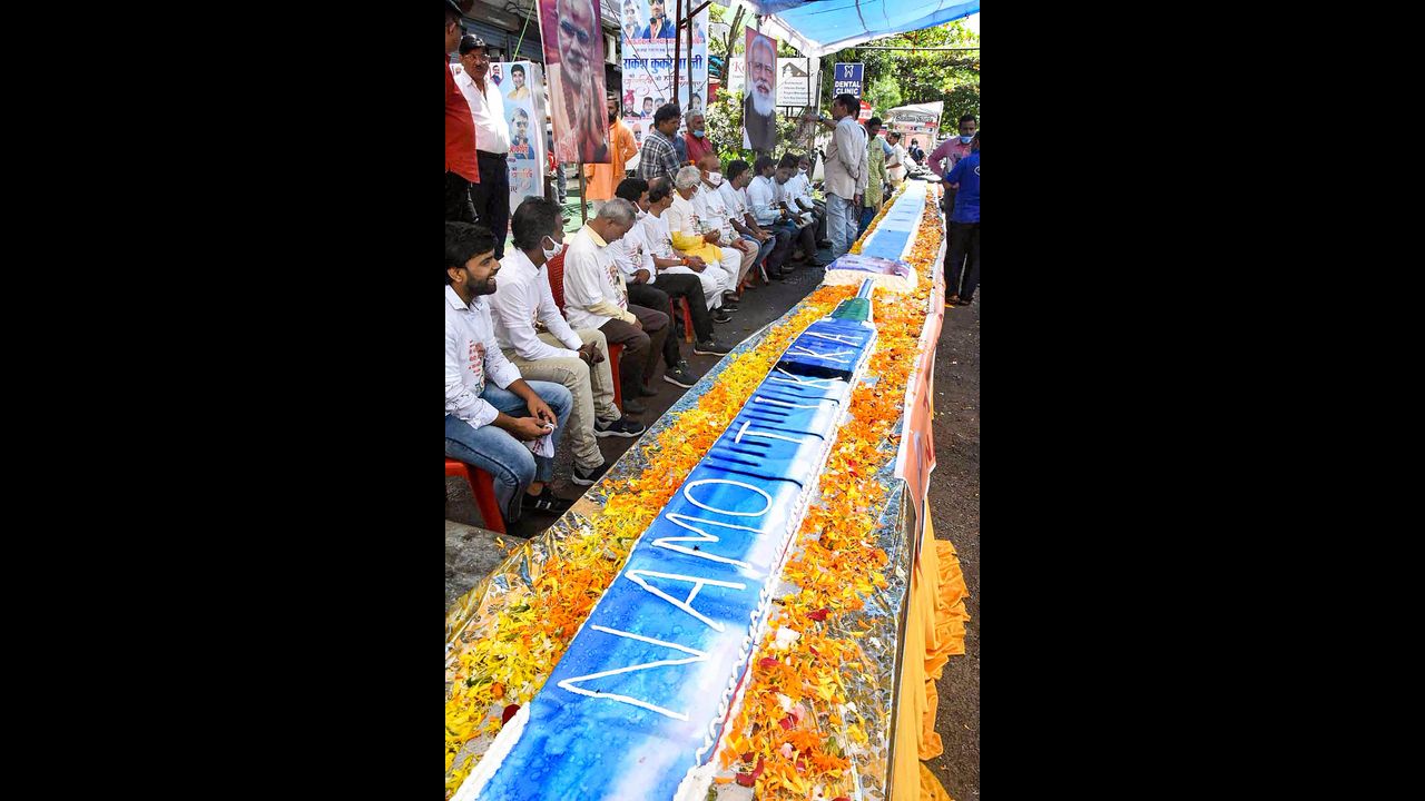 BJP workers sit beside a vaccine shaped cake on the eve of the birthday of Prime Minister Narendra Modi, in Bhopal. Pic/PTI