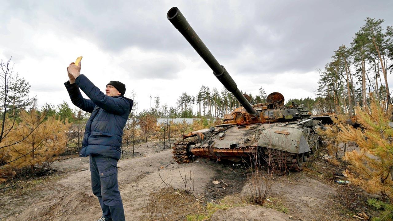 A man takes a selfie in front of a destroyed Russian tank in the village of Andriivka on Sunday