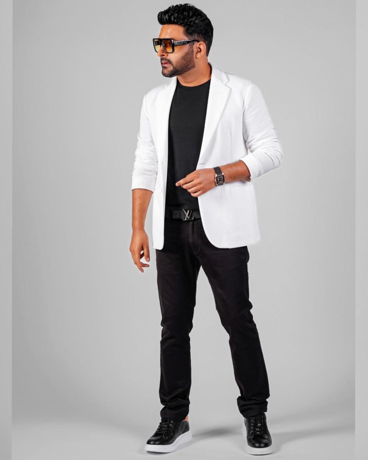 Kapil Sharma has turned a new leaf, physically as he recently falunted his new style. In the picture, Kapil can be seen wearing a black T-shirt and black trousers. He styled it with a white blazer, sunglasses, and sneakers. He credited his wife Ginni Chatrath as his stylist