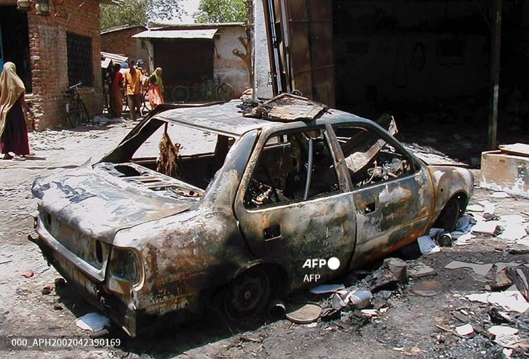 Residents walk past a car burnt by rioters in the Khanpur area of Ahmedabad on April 23, 2002