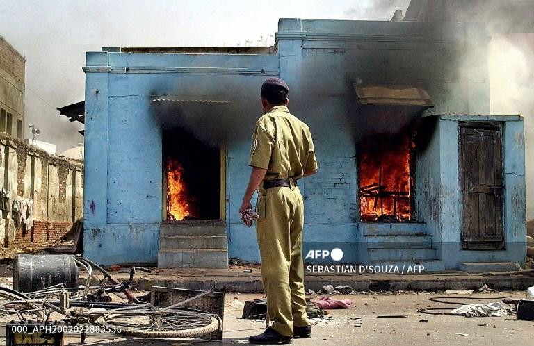 A policeman looks at burning shops at the entrance of a mosque in Ahmedabad on February 28, 2002