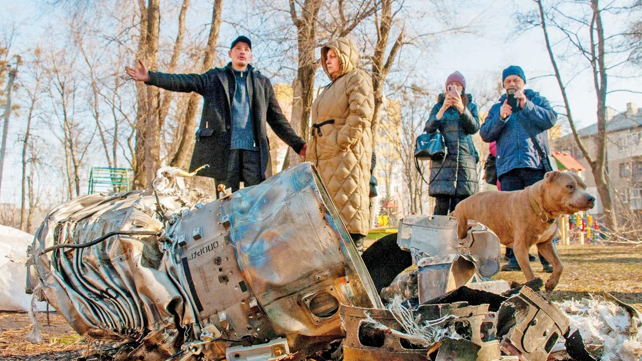 People stand near damaged military equipment on the street in the aftermath of an apparent Russian strike in Kharkiv
