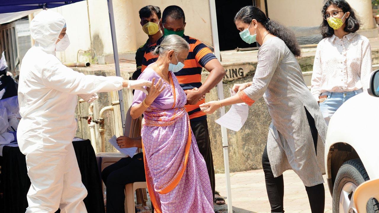 A doctor helps a senior citizen walk to the camp to get tested for COVID-19, at Thakur Complex, Kandivli. File pic