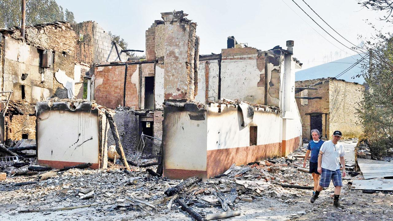 Villagers walk past burnt houses in A Veiga de Cascalla, northern Spain, on Tuesday. Pics/AP, AFP