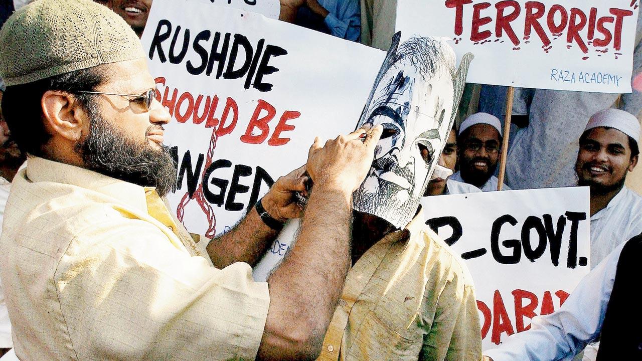 A file photograph of a protester blackening a mask of writer Salman Rushdie, condemning his stay in Mumbai, in January 2004. Rushdie was alleged to have made remarks against Prophet Mohammed in The Satanic Verses. Pic/Getty Images