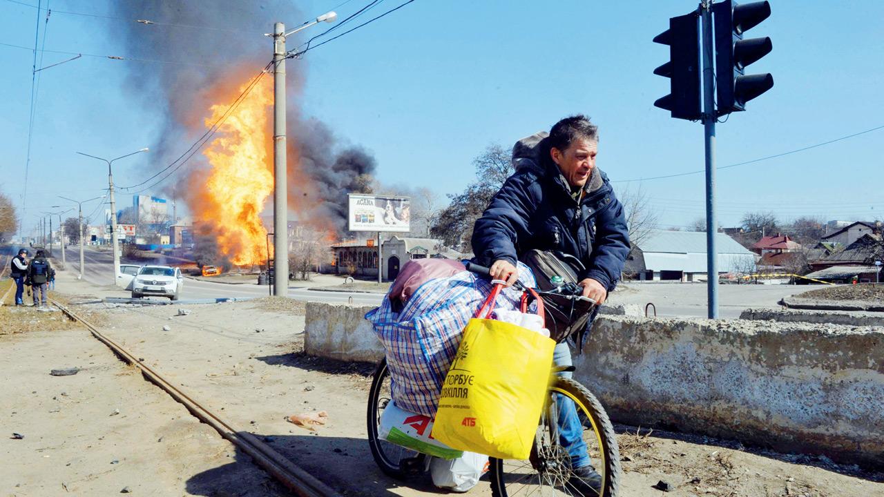A man carries a bicycle with his belongings as fire engulfs a gas station following an artillery attack on the 30th day of the Russian invasion of Ukraine in the northeastern city of Kharkiv. Pic/AFP
