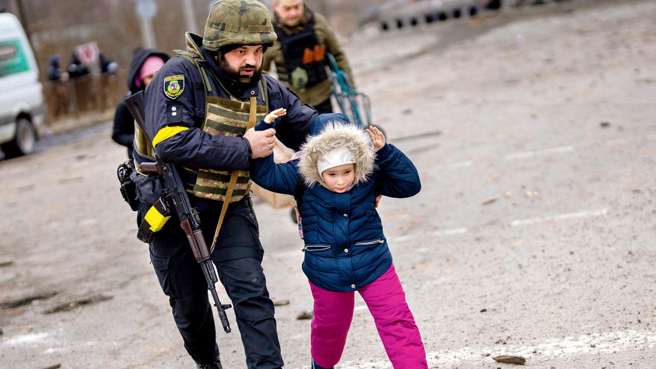 A Ukrainian police officer runs while holding a child as the artillery echoes nearby, in Irpin near Kyiv on Monday. Pic/AP