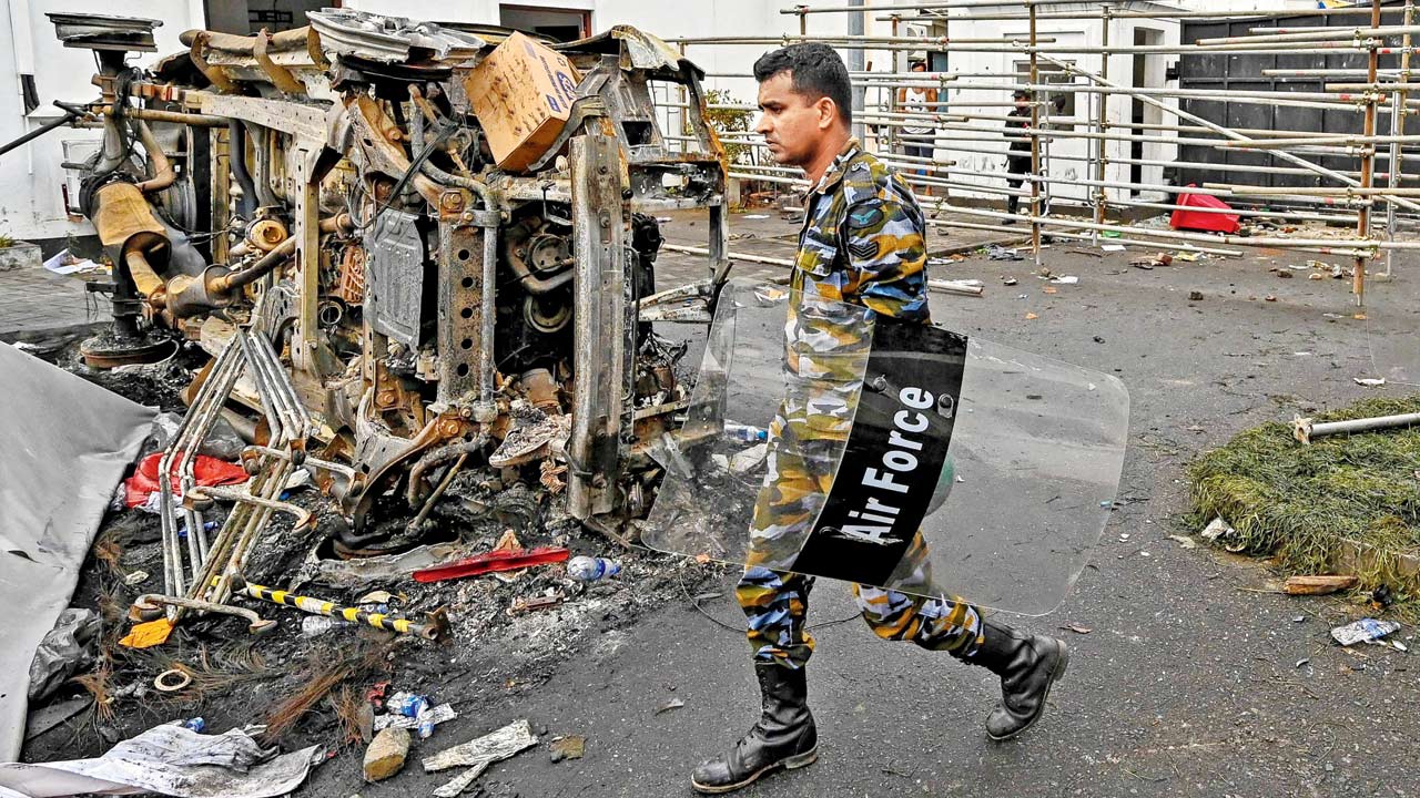 A security personnel walks past a burned vehicle near ex-PM Mahinda Rajapaksa’s official residence, in Colombo on Tuesday