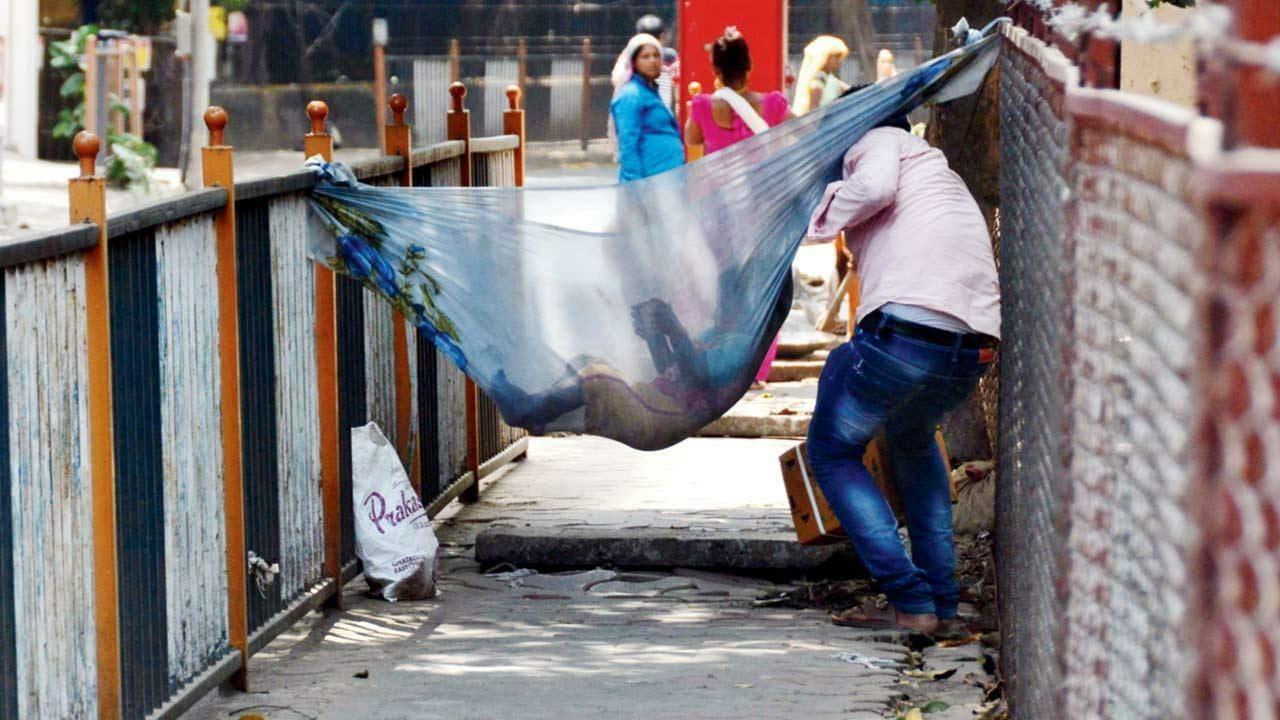 In its happy cocoon: A child remains engrossed in its virtual world while people find a way past his makeshift hammock on a pavement in Chembur East. Pic/Sayyed Sameer Abedi