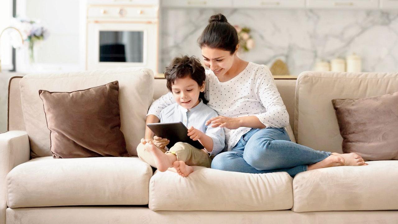 A mother sits with her child as they play a digital game