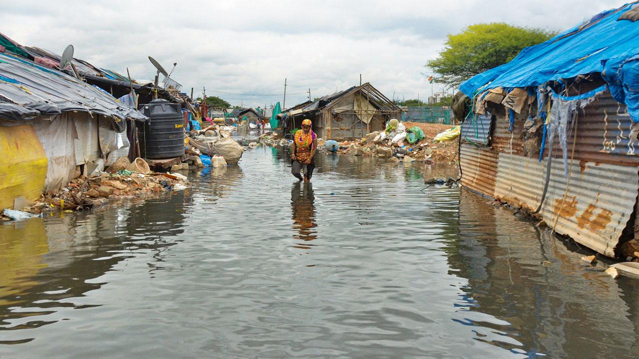 A woman walks through a waterlogged slum area, in Bengaluru, on Thursday. Pic/PTI