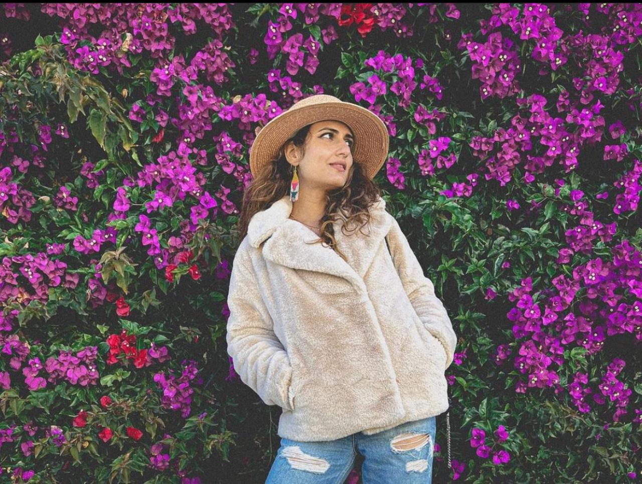 In her second look, the diva clicked an alluring picture of herself posing in the abode of nature adorned with pink flowers. She chose to style herself with a furry Blazer along with ripped jeans
